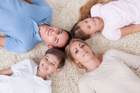 Close-up Of Happy Family Lying On Carpet Looking Up Heads Together At Homeの写真素材