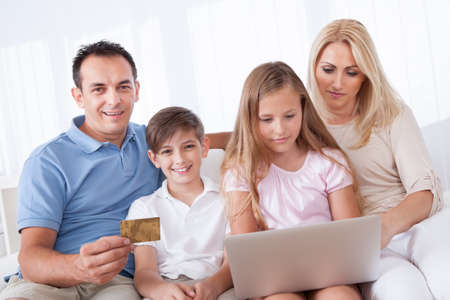 A Happy Family With Two Children Sitting On A Sofa Shopping Using Laptop At Homeの写真素材