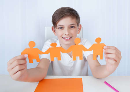 Portrait Of Boy Holding Figures Of Paper Family In Hand At Homeの写真素材