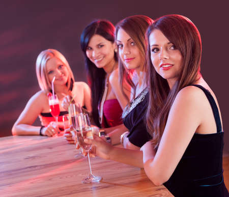 Four attractive young lounge ladies seated at a bar counter in a nightclub enjoying cocktails togetherの写真素材