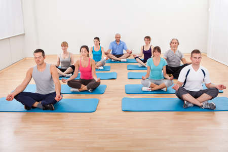 Diverse group of people practicing yoga in a gym sitting cross-legged on their mats meditatingの写真素材