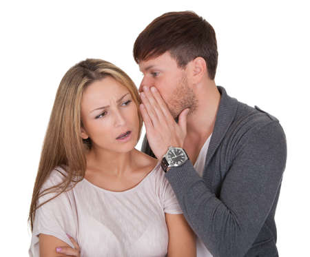 Man whispering in a woman ear with his hand shielding his mouth as he shares a confidence with her...