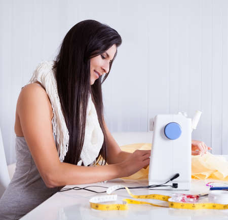 Smiling young woman or seamstress working with her sewing machine stitching a long length of fabric