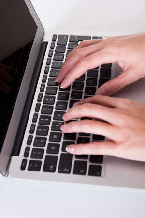 High angle cropped view image of female hands typing on a laptop keyboard with a blank white screenの写真素材