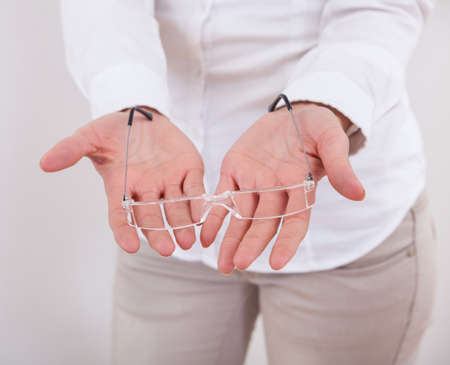 Beautiful young smiling woman holding a pair of modern spectacles in her cupped hands isolated on whiteの写真素材