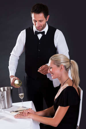 Waiter serving champagne to a beautiful blonde woman seated at a table in an elegant restaurantの写真素材