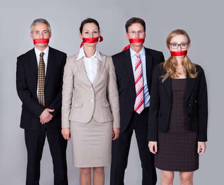 Businesspeople bound by red tape around their mouths standing in a row unable to speak or divulge informationの写真素材