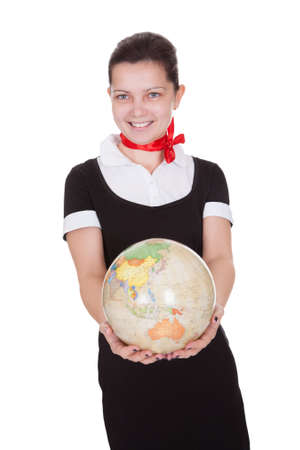 Pretty flight attendant in a stylish uniform holding a globe in a travel and tourism conceptの写真素材