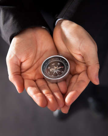 Businessman looking at a compass which he is holding in his hand with focus to the compassの写真素材