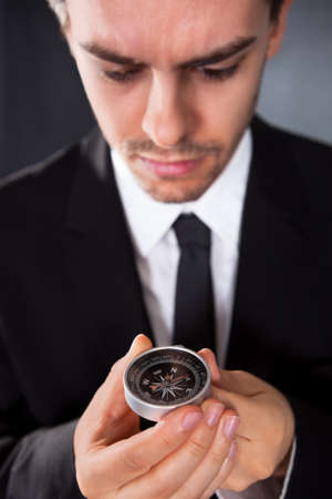 Businessman looking at a compass which he is holding in his hand with focus to the compassの写真素材