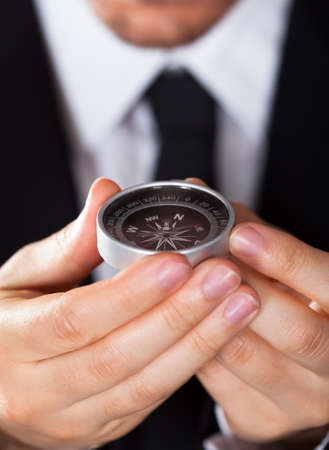Businessman looking at a compass which he is holding in his hand with focus to the compassの写真素材
