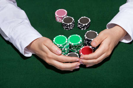 Croupier collecting in the bets at a casino table with his hands encircling various stacks of tokens...