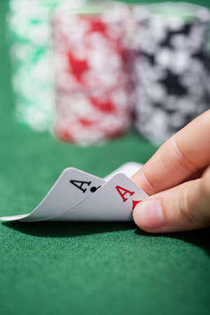 Hand of a male poker player lifting the corners of two cards on the green felt checking a pair of...