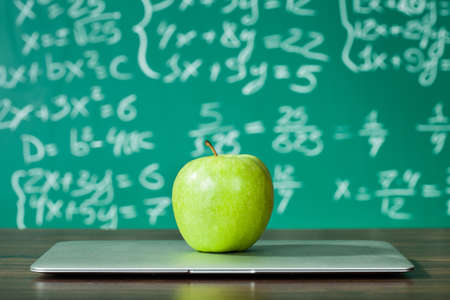 Laptop and apple on the desk in front of blackboardの写真素材