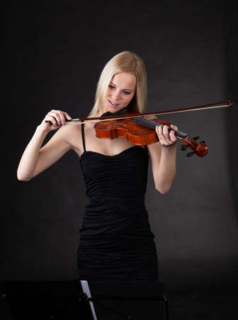 Beautiful young woman playing violin over black backgroundの写真素材