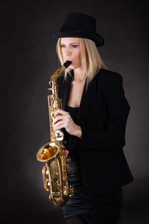 Beautiful young woman playing saxophone over black backgroundの写真素材
