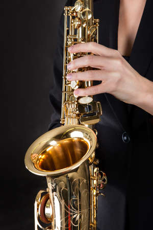 Beautiful young woman playing saxophone over black backgroundの写真素材