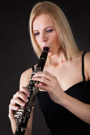 Beautiful young woman playing clarinet over black backgroundの写真素材