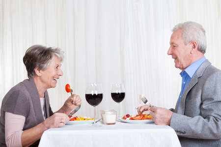 Portrait Of Senior Couple With Wine Glasses Sitting At A Restaurantの写真素材