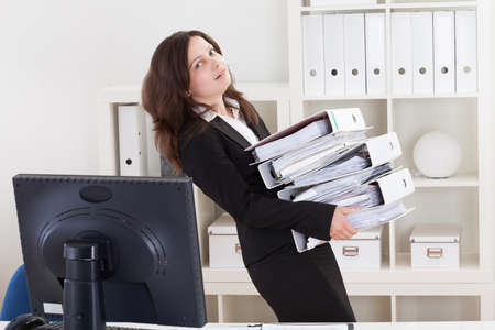 Businesswoman Carrying Stack Of Folders In Office