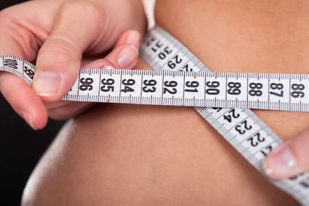 Beautiful Slim Woman Measuring Her Waistline With A Measuring Tapeの写真素材