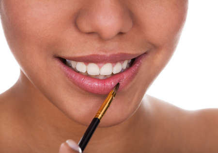 Young Woman Applying Lipstick Over White Backgroundの写真素材