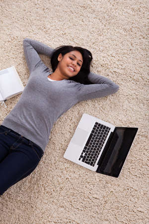 Top View Of Young Woman Lying On Carpet With Laptop