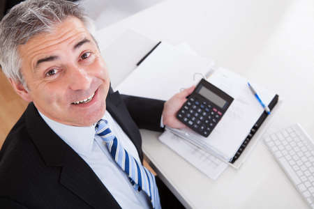 Portrait Of Mature Businessman Calculating Finance At Officeの写真素材