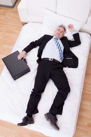 Portrait Of Thoughtful Mature Businessman Relaxing On Bedの写真素材