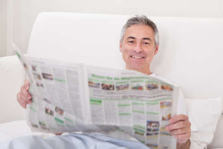 Portrait Of Happy Mature Man Holding Newspaperの写真素材