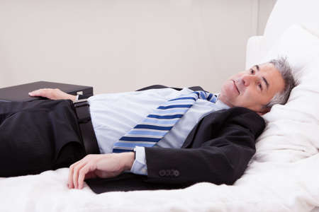 Portrait Of Thoughtful Mature Businessman Relaxing On Bedの写真素材