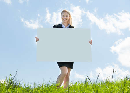 Young Businesswoman Sitting In Field Holding Placardの写真素材