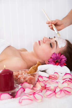 Beautiful young woman getting facial mask at spa studioの写真素材