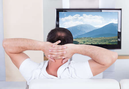Portrait of man sitting on couch watching televisionの写真素材