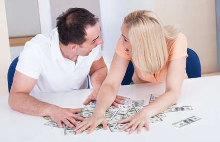 Excited Couple Looking At Each Other Collecting Money On Deskの写真素材