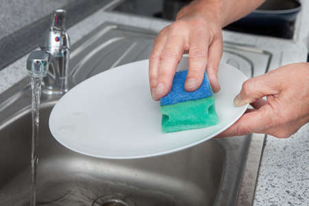 Close-up Of Hand Cleaning Plate With Scrubberの写真素材