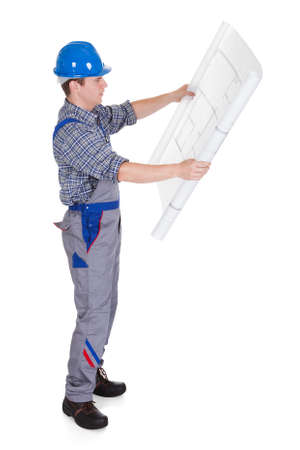 Male construction worker looking at blue prints isolated on white backgroundの写真素材