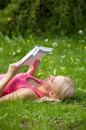 Happy Young Beautiful Woman Lying On Grass Reading Bookの写真素材