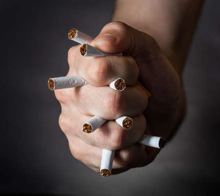 Male Fist Piercing Cigarettes Over Black Backgroundの写真素材