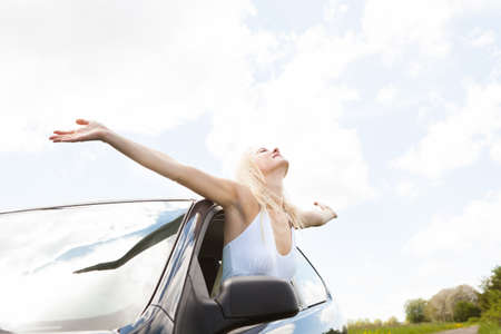Happy Young Woman Raising Hand Out Of Car Windowの写真素材
