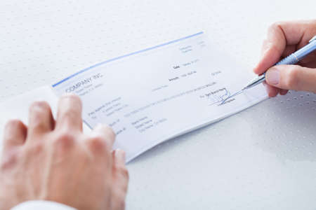 A Male Hand Filling Out The Amount On A Cheque