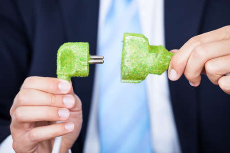 Close-up Of Businessman Holding Grass Covered Electric Plug And Socket