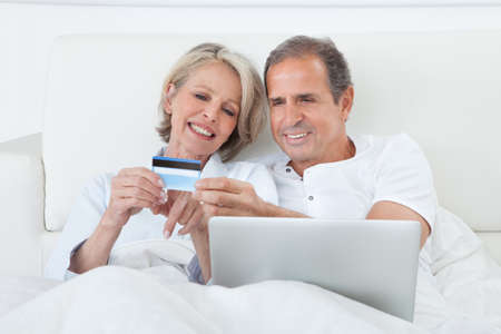 Couple In Bedroom Shopping Online Holding Credit Card