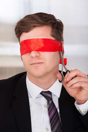 Businessman cutting his blindfold with scissor in officeの写真素材