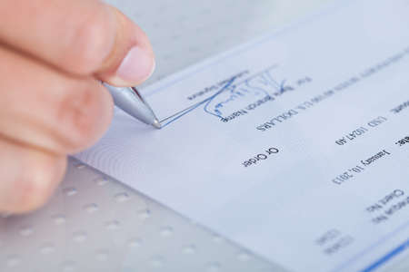 A Male Hand Filling Out The Amount On A Cheque
