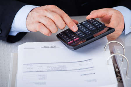 Happy Mature Businessman Calculating Finance With Calculator At Desk