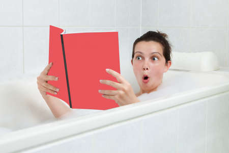 Portrait of happy young woman in bathtub reading book