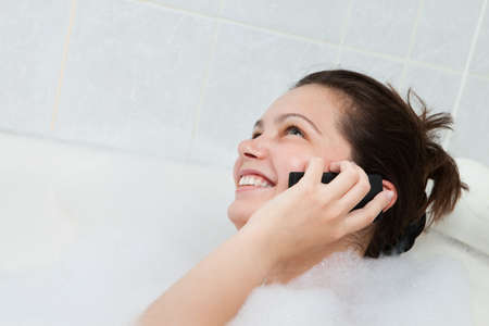 Happy young woman in bathtub talking on mobile