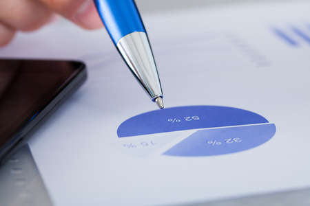 Close-up Of Hand Holding Pen Over Graph