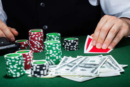 Portrait of a croupier looking at playing cards with gun and stack of token chips on tableの写真素材
